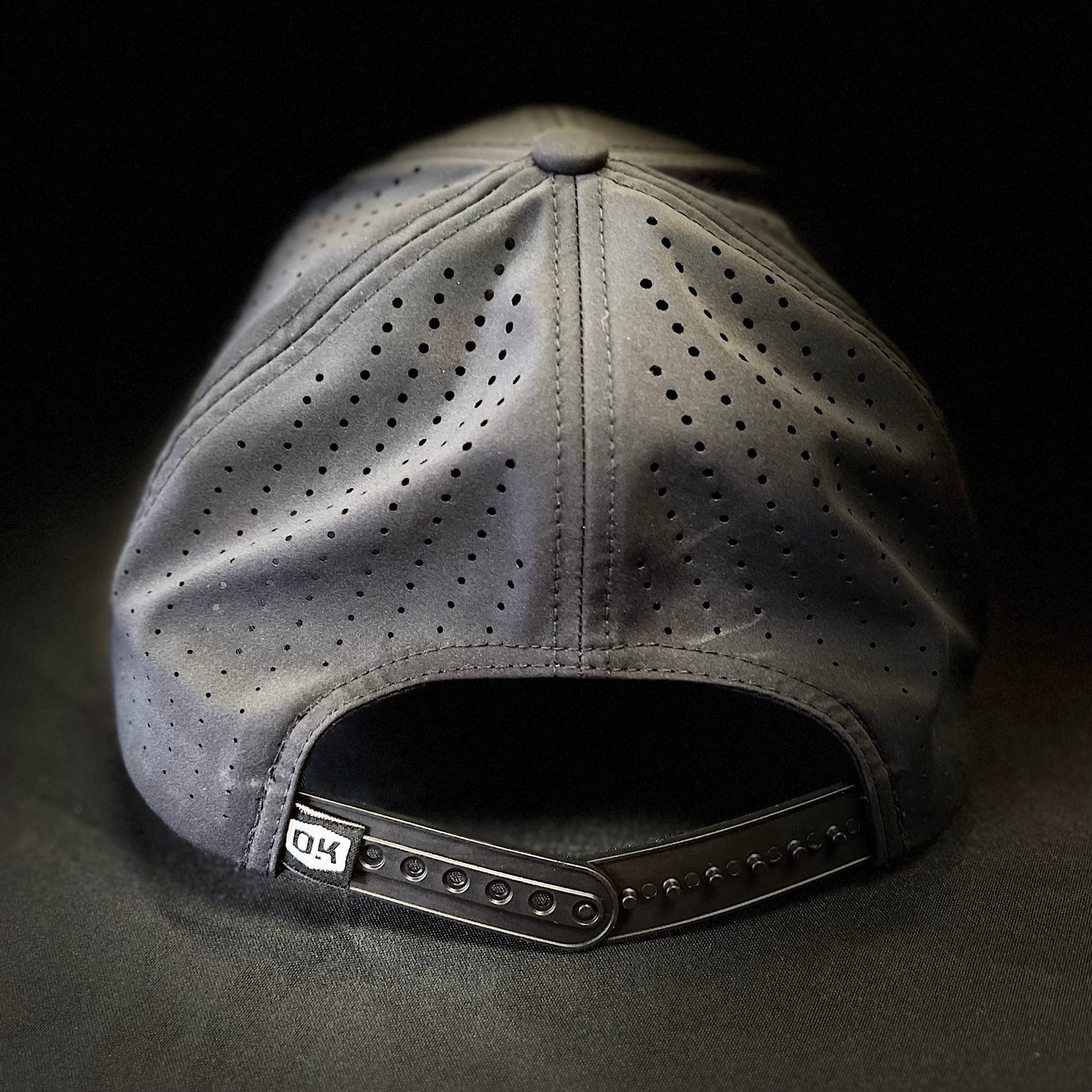 Back view of the JRW x OKIE Black Magic golf hat showing the adjustable snapback closure and OKIE logo tag, set against the black mesh for a balanced street-meets-sport aesthetic.